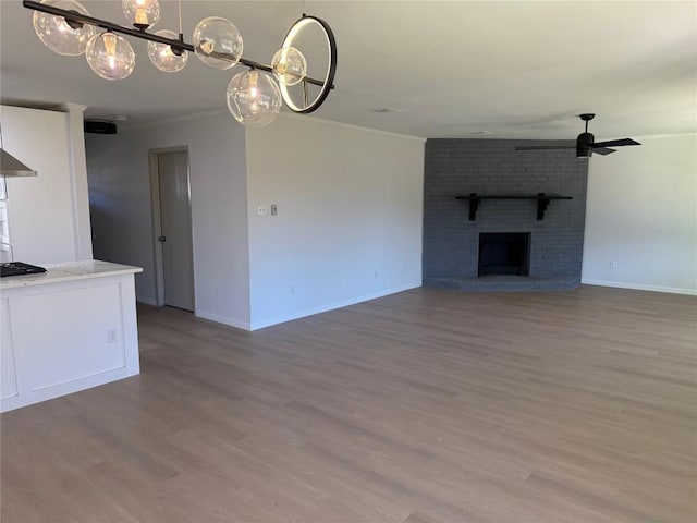 unfurnished living room featuring hardwood / wood-style floors, ceiling fan with notable chandelier, a brick fireplace, and ornamental molding