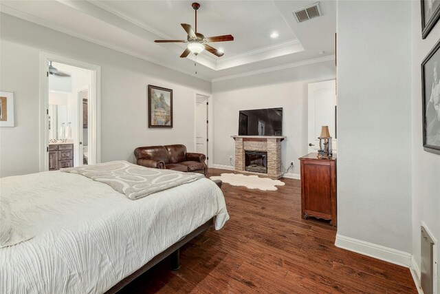 bedroom featuring connected bathroom, ceiling fan, dark wood-type flooring, a stone fireplace, and a tray ceiling