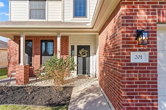 entrance to property with an attached garage, covered porch, roof with shingles, and brick siding