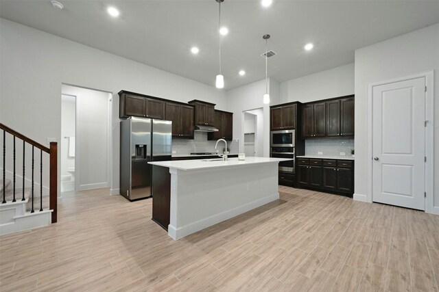 kitchen featuring dark brown cabinetry, backsplash, pendant lighting, a kitchen island with sink, and appliances with stainless steel finishes