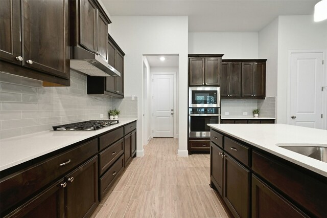 kitchen with stainless steel gas stovetop, backsplash, light wood-type flooring, built in microwave, and dark brown cabinetry