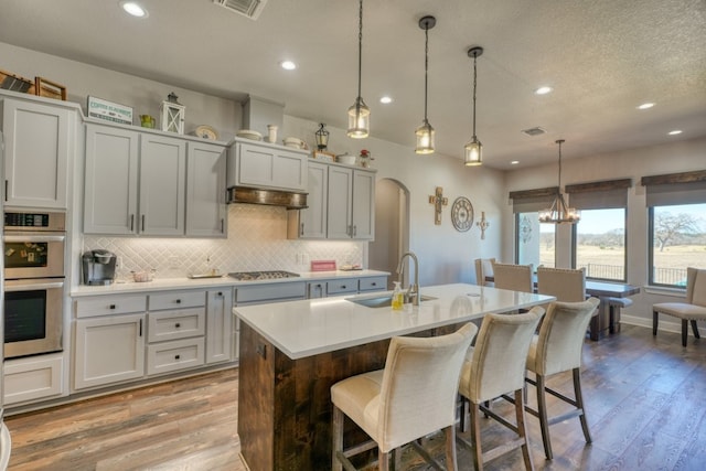 kitchen with a kitchen bar, sink, decorative light fixtures, light hardwood / wood-style flooring, and a center island with sink