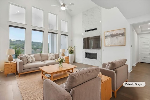 living room with a tile fireplace, ceiling fan, a towering ceiling, and wood-type flooring