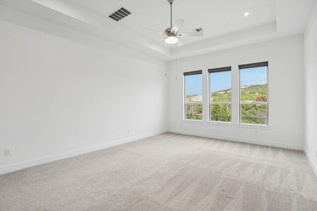 empty room featuring a tray ceiling, ceiling fan, and light colored carpet