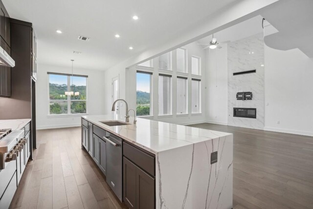 kitchen featuring sink, dark hardwood / wood-style floors, a fireplace, an island with sink, and light stone counters