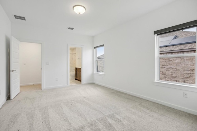 unfurnished bedroom featuring light colored carpet and ensuite bath