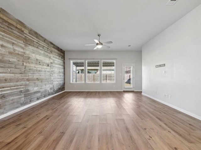 unfurnished room with ceiling fan, wooden walls, and light hardwood / wood-style flooring