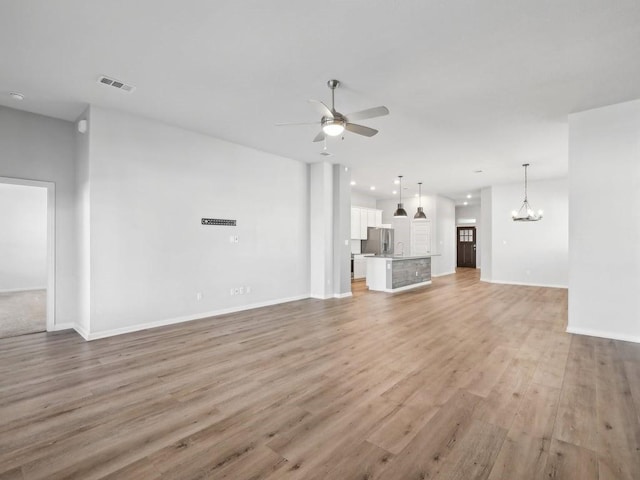 unfurnished living room with light hardwood / wood-style flooring, ceiling fan with notable chandelier, and sink