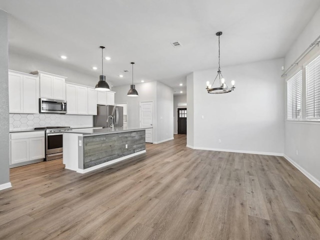 kitchen with tasteful backsplash, stainless steel appliances, decorative light fixtures, white cabinets, and an island with sink