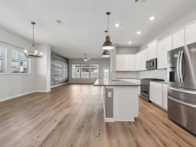 kitchen with sink, pendant lighting, a kitchen island with sink, ceiling fan with notable chandelier, and appliances with stainless steel finishes