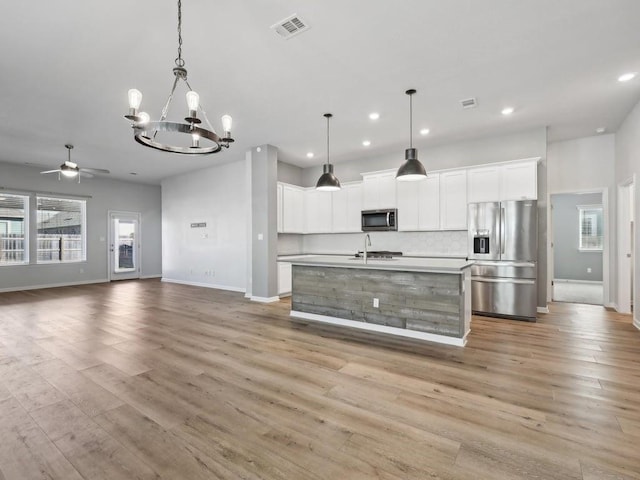 kitchen featuring white cabinets, decorative light fixtures, stainless steel appliances, and a kitchen island with sink