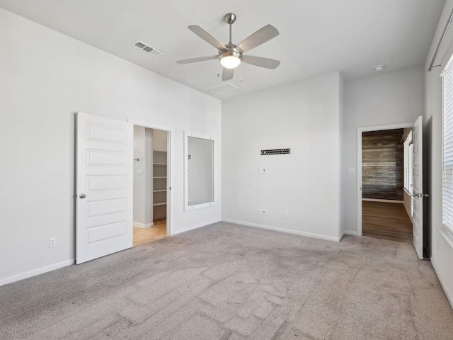 unfurnished bedroom with ceiling fan, a walk in closet, light carpet, and a closet