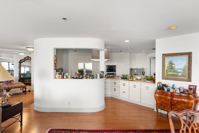 kitchen with kitchen peninsula, appliances with stainless steel finishes, backsplash, light hardwood / wood-style flooring, and white cabinets