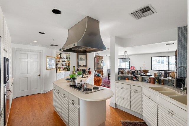 kitchen with white cabinets, appliances with stainless steel finishes, island range hood, and light hardwood / wood-style floors