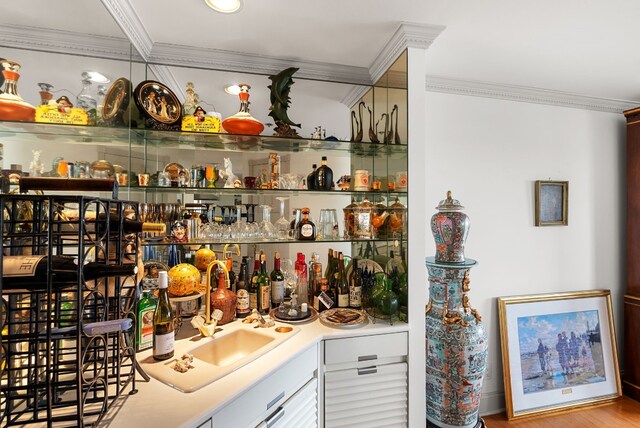 bar with sink, light hardwood / wood-style flooring, and ornamental molding