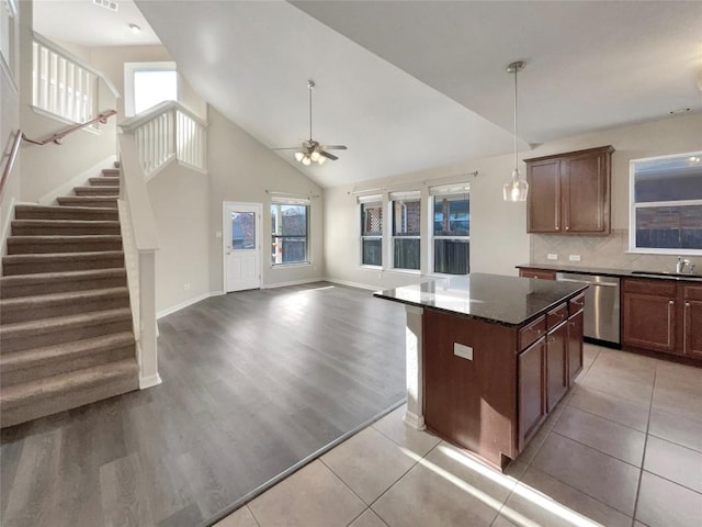 kitchen featuring backsplash, stainless steel dishwasher, ceiling fan, dark stone countertops, and a kitchen island