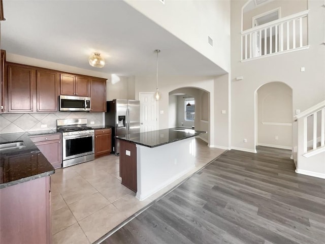 kitchen with backsplash, dark stone countertops, stainless steel appliances, and hanging light fixtures