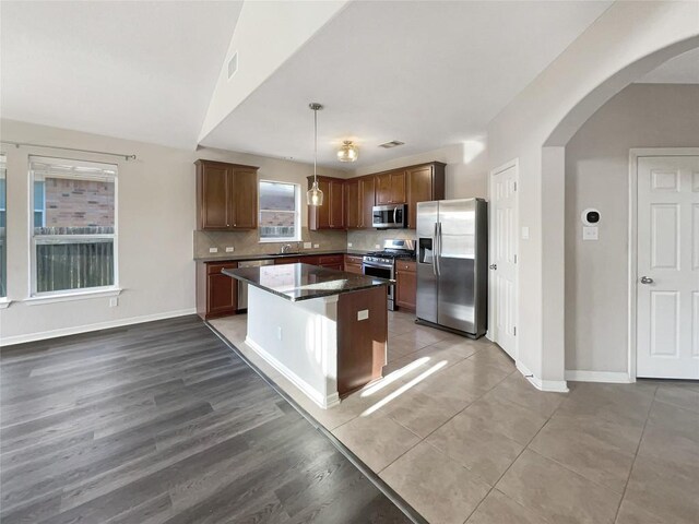 kitchen featuring stainless steel appliances, lofted ceiling, decorative light fixtures, decorative backsplash, and a kitchen island