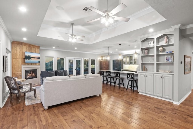 living room featuring ornamental molding, a tray ceiling, a fireplace, and light wood-style flooring