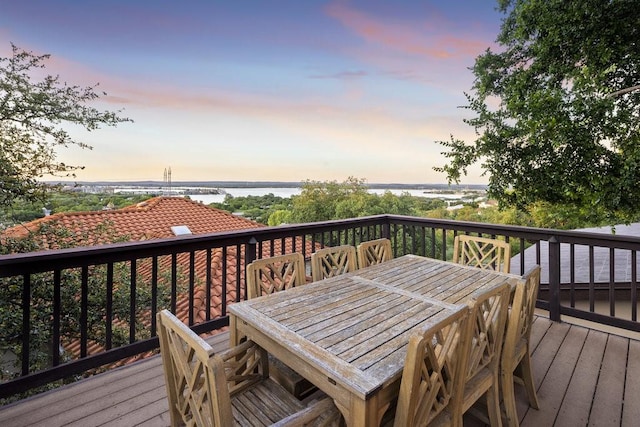 deck at dusk with outdoor dining space and a water view