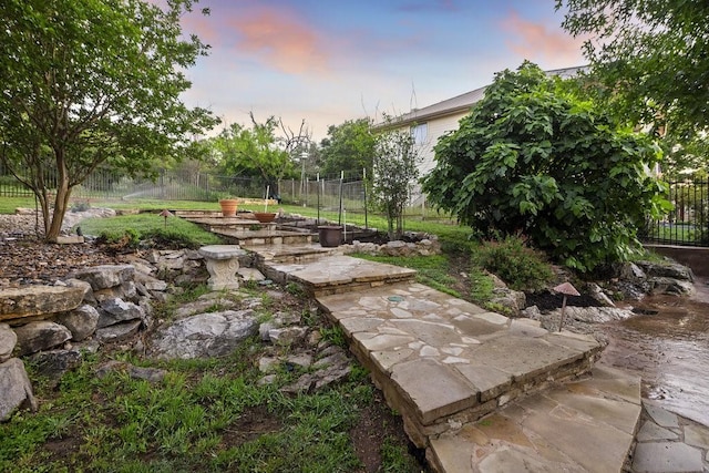 yard at dusk featuring a garden and fence