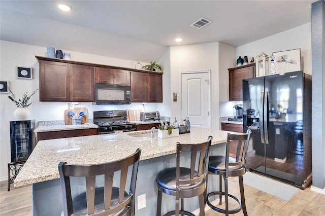 kitchen featuring dark brown cabinets, light hardwood / wood-style floors, a center island with sink, and black appliances