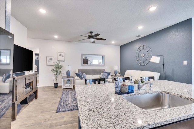 kitchen featuring light stone countertops, a textured ceiling, light hardwood / wood-style floors, sink, and ceiling fan