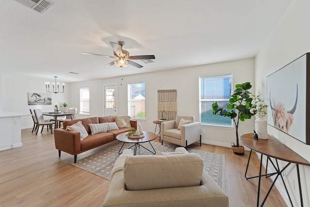 living room featuring light wood-type flooring, ceiling fan with notable chandelier, and a wealth of natural light