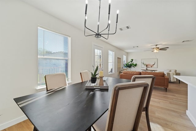 dining space with ceiling fan with notable chandelier and light wood-type flooring