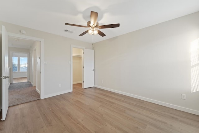 unfurnished bedroom with a closet, a walk in closet, light hardwood / wood-style floors, and ceiling fan