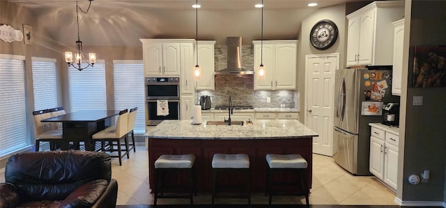 kitchen featuring decorative light fixtures, white cabinets, stainless steel appliances, decorative backsplash, and wall chimney range hood