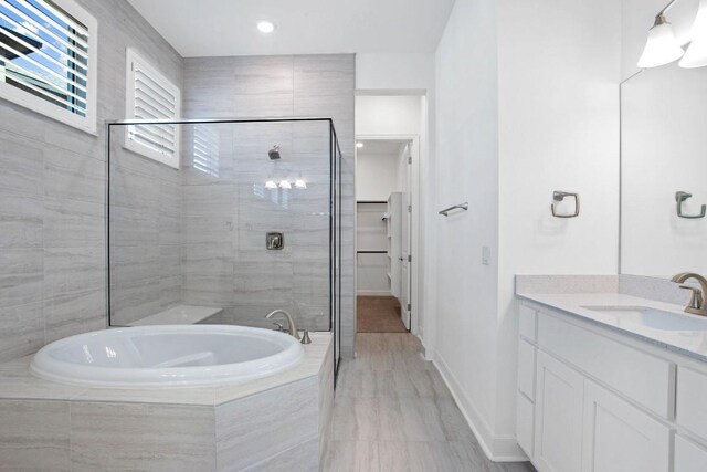 full bathroom featuring a stall shower, vanity, a bath, and baseboards