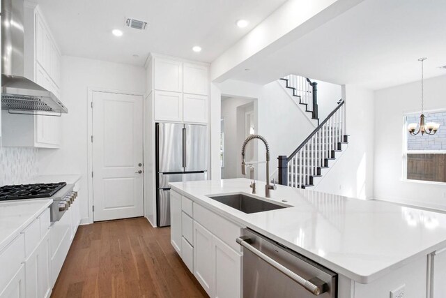 kitchen featuring dark wood-style floors, appliances with stainless steel finishes, wall chimney range hood, a chandelier, and a sink