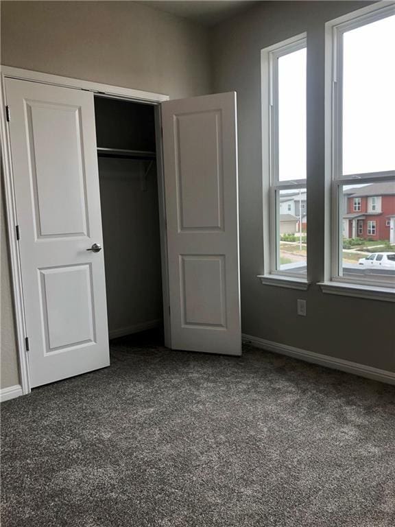 unfurnished bedroom with dark colored carpet, a closet, and multiple windows