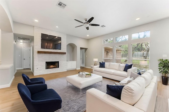 living room with a stone fireplace, ceiling fan, and light wood-type flooring