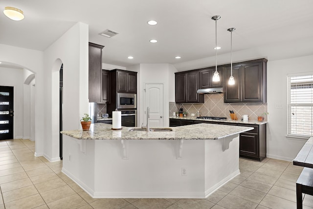 kitchen with stainless steel appliances, backsplash, hanging light fixtures, light stone countertops, and sink