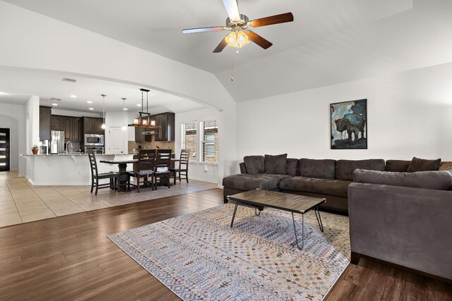 living room with ceiling fan, light wood-type flooring, sink, and lofted ceiling