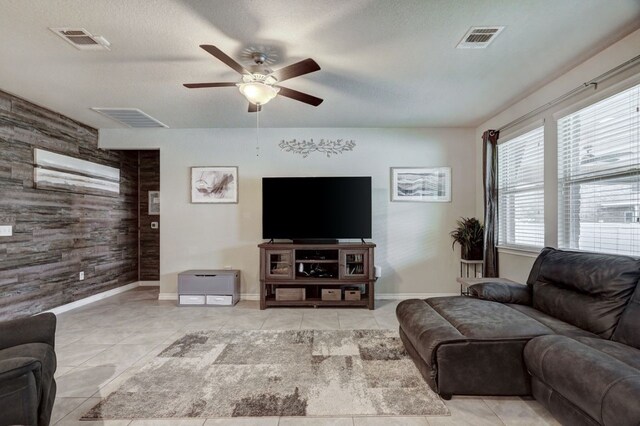 tiled living room featuring wood walls, a textured ceiling, and ceiling fan