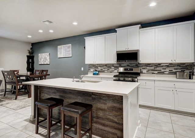 kitchen featuring sink, light tile patterned floors, appliances with stainless steel finishes, white cabinetry, and a center island with sink