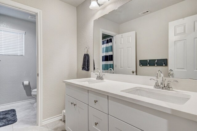 full bath featuring toilet, double vanity, visible vents, and a sink