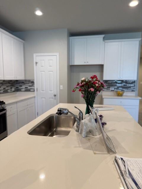 kitchen with sink, stainless steel range, white cabinets, and backsplash