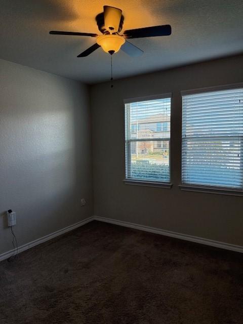 empty room featuring dark carpet, a ceiling fan, and baseboards