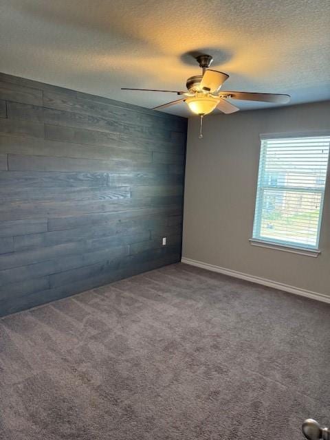 spare room with carpet, wooden walls, baseboards, and a textured ceiling