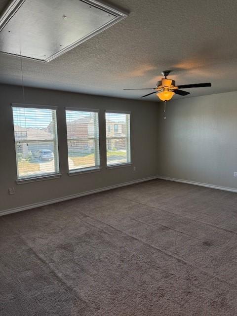 spare room with a textured ceiling, a ceiling fan, baseboards, dark colored carpet, and attic access