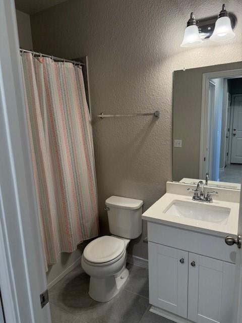 full bath featuring a textured wall, toilet, vanity, baseboards, and tile patterned floors