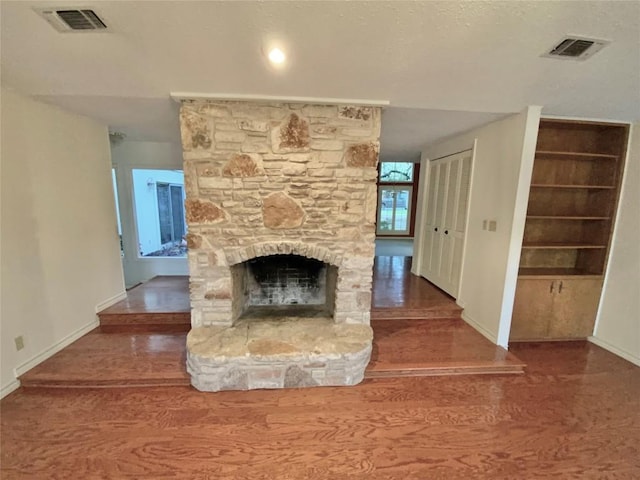 unfurnished living room with built in features, hardwood / wood-style floors, and a stone fireplace