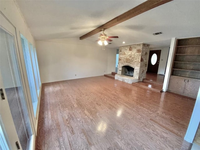 unfurnished living room with vaulted ceiling with beams, ceiling fan, a stone fireplace, and hardwood / wood-style flooring