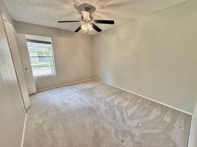 spare room with light carpet, a ceiling fan, a textured ceiling, and baseboards