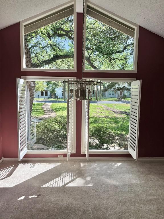 doorway with carpet floors, a textured ceiling, lofted ceiling, and baseboards