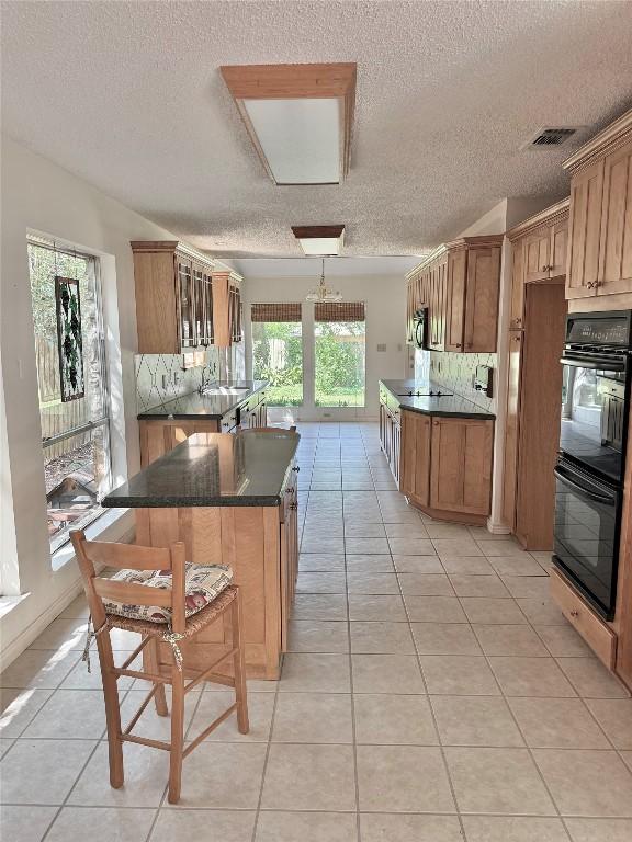 kitchen with a textured ceiling, dark countertops, backsplash, black appliances, and light tile patterned floors